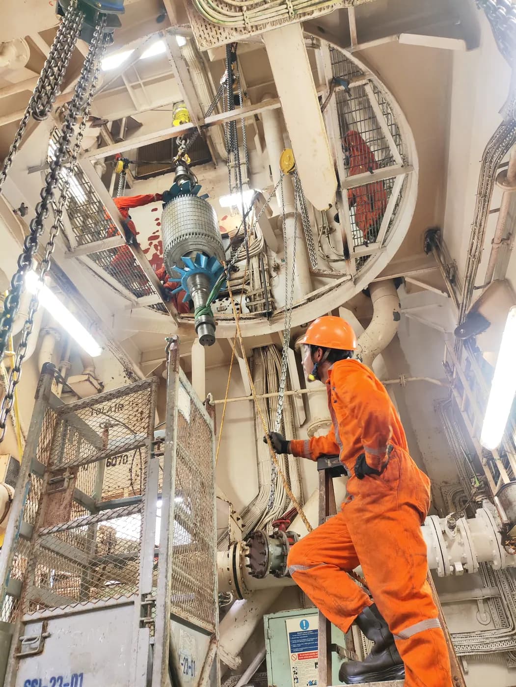 Técnico con overol naranja subiendo una escalera en la sala de máquinas de una embarcación